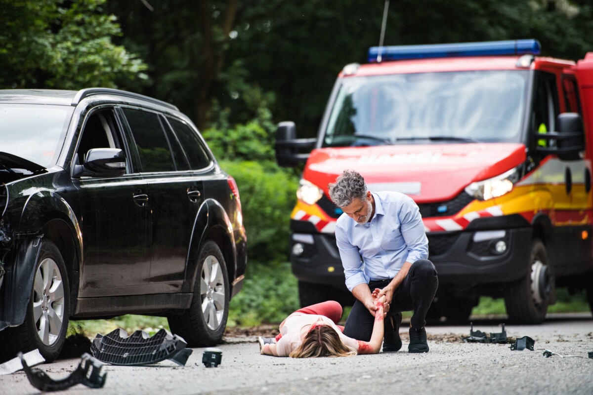 A man helping a young woman lying unconscious on the road after a car accident Personal Injury Lawyer