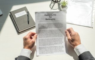 Cropped view of businessman holding petition for bankruptcy near notebook on white textured