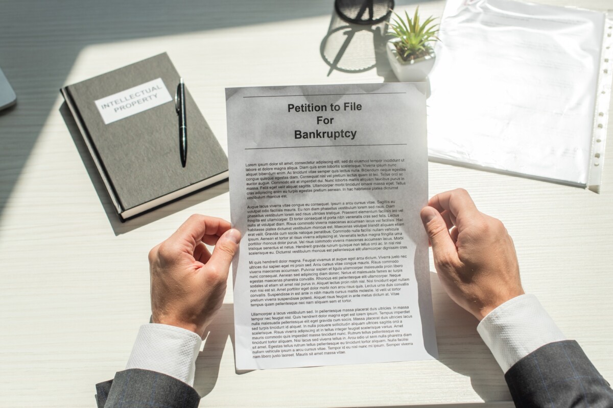 Cropped view of businessman holding petition for bankruptcy near notebook on white textured
