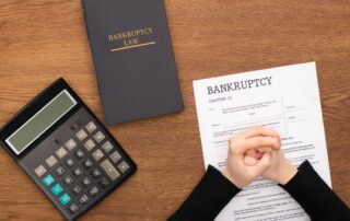 cropped view of female clenched hands on bankruptcy paper near bankruptcy law book and calculator on