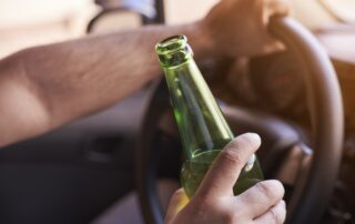 Man driving a car while holding a bottle of beer. Drunk diving, unsafe driving concept