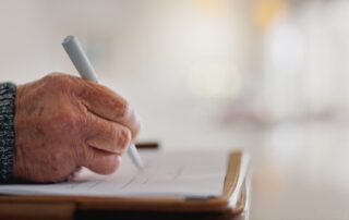 Senior person, hands and signature on will in home, insurance paperwork and plan for title deed. Fi