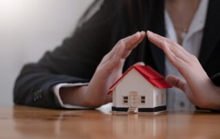 Protect your house concept. Small toy house covered by hands