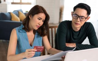 serious Asian wife checking analyzing statement utilities bills sitting together at home.