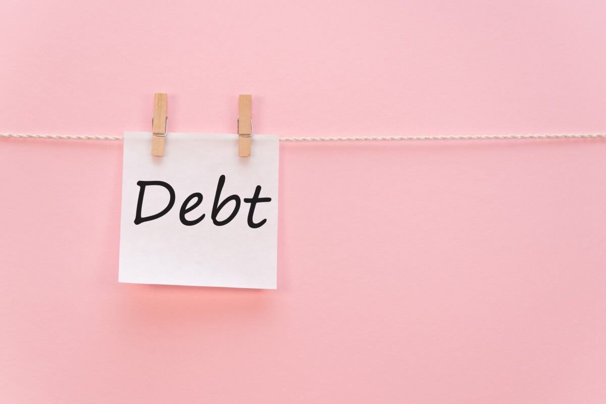 sticker with the inscription Debt hangs with a clothespin on a rope on a pink background