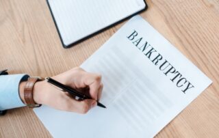 top view of man holding pen near paper with bankruptcy letters and notebook